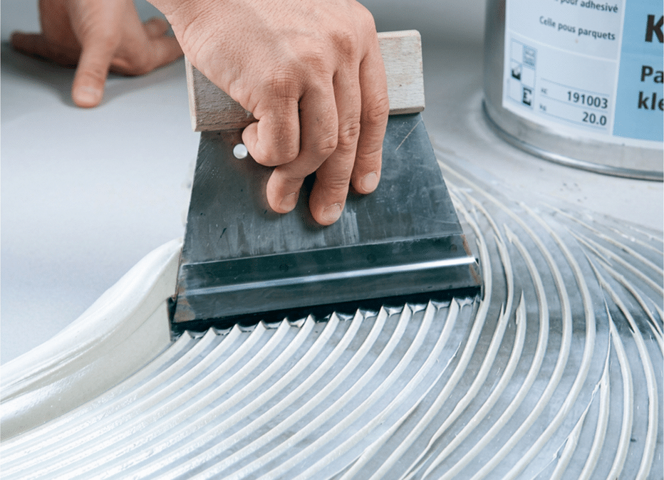 applying floor adhesive to subfloor using adhesive pail on jobsite
