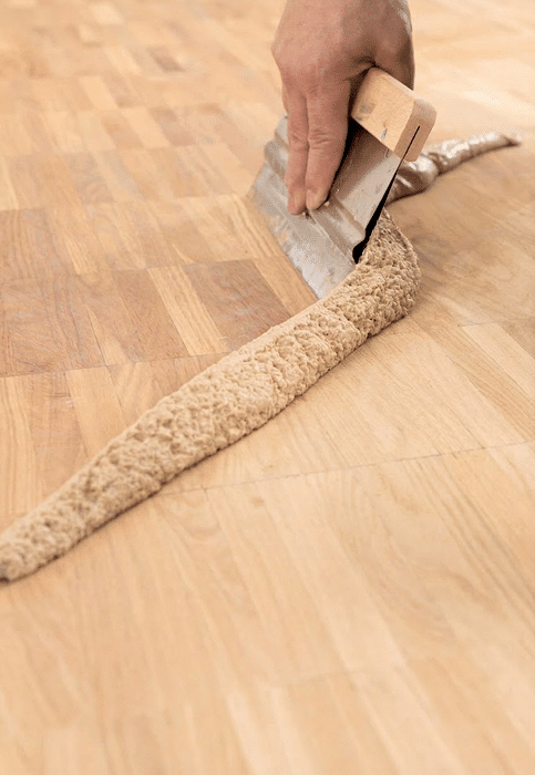 finisher using a steel trowel to spread hardwood finish on a floor