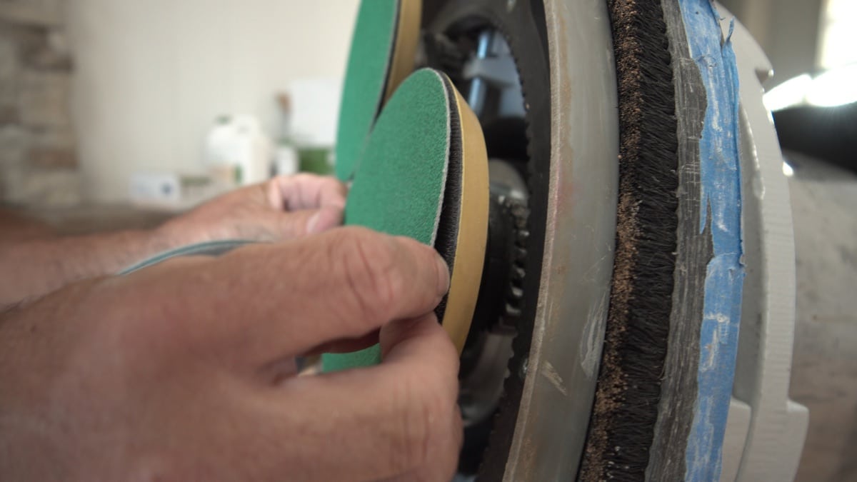 a finisher changing a green abrasive disc on a multidisc sander head